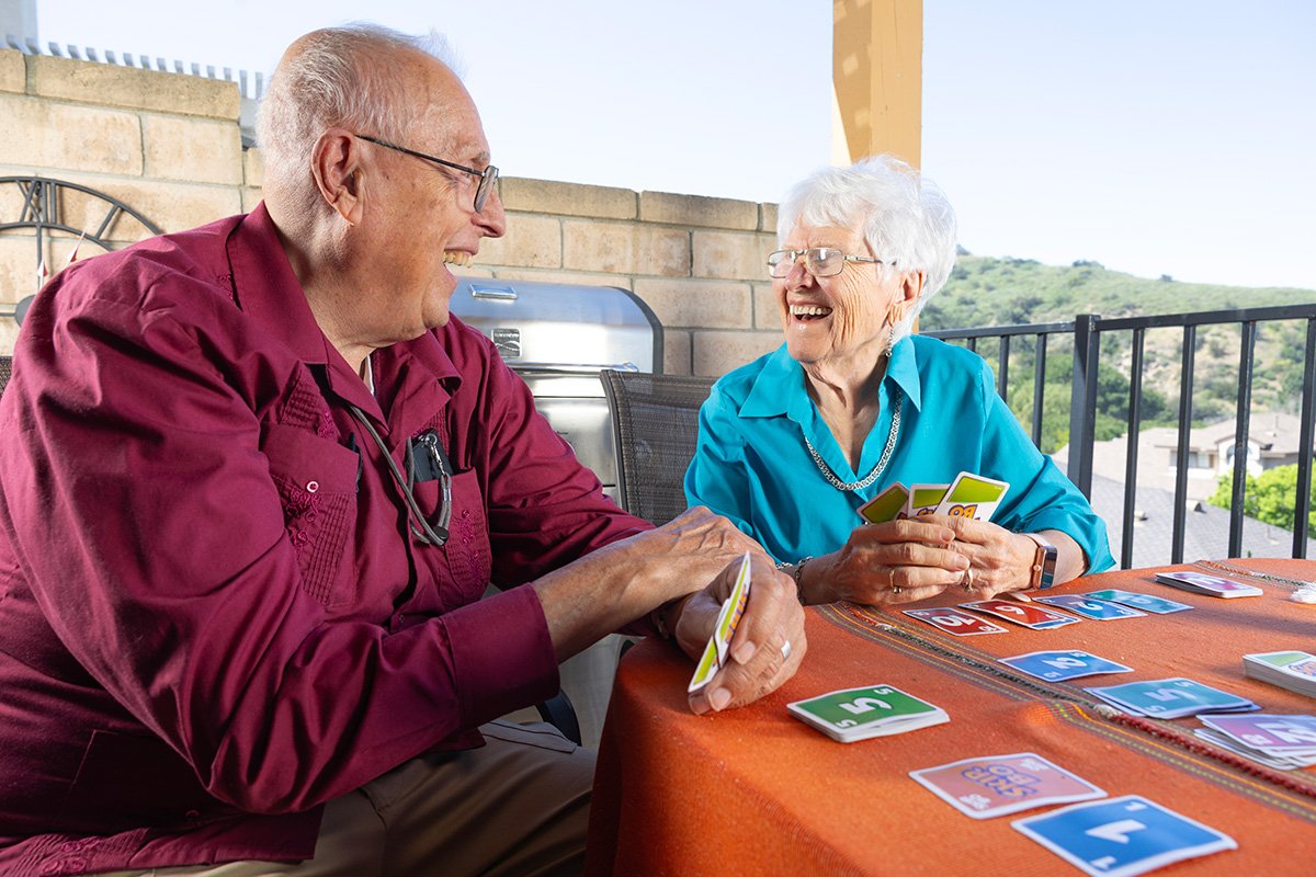 DP3A9209 An elderly couple sitting at a table playing a card game and laughing.